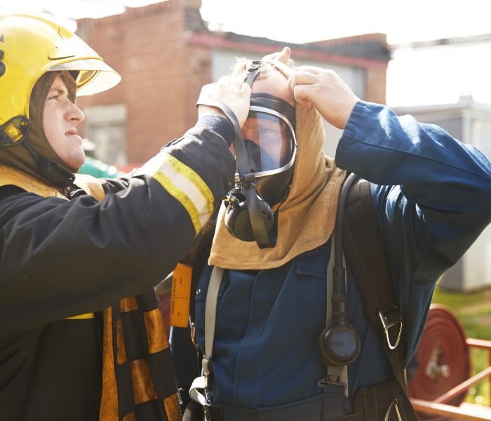 Firemen training, supervisor helping fireman with breathing apparatus at training facility Firemen training, supervisor helping fireman with breathing apparatus at training facility