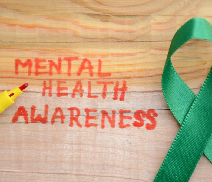Lettering “MENTAL HEALTH AWARENESS” and green ribbon on the wooden surface Red lettering "MENTAL HEALTH AWARENESS" and green ribbon on the wooden surface