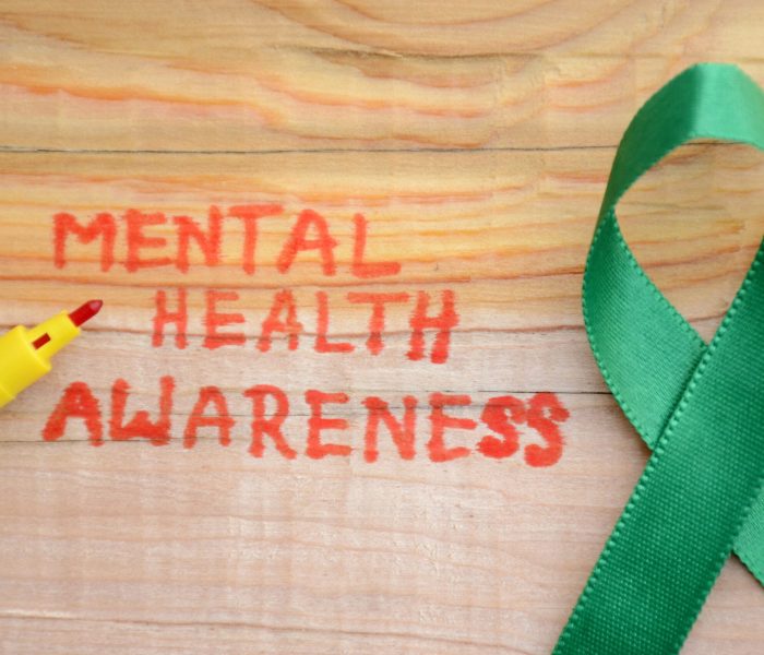 Red lettering "MENTAL HEALTH AWARENESS" and green ribbon on the wooden surface